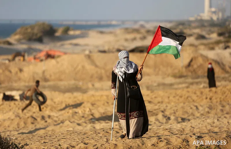A Palestinian woman on crutches waves the national flag during clashes with Israeli forces in a demonstration against the Israeli blockade on Gaza Strip, along the Gaza sea barrier on the maritime border with Israel near...