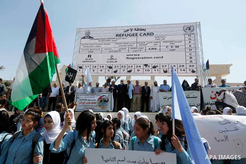 Palestinian protesters gather in front of a fabiricated giant refugee card attributed to their President Mahmud Abbas, during a protest against the United States decision earlier this year to stop funding and backing the...