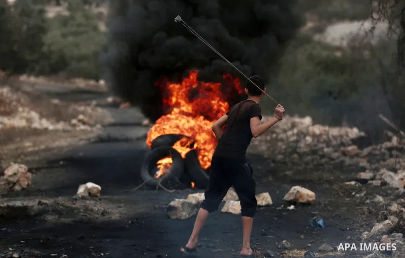 A Palestinian protester uses a slingshot to hurl stones towards Israeli troops during clashes against Israel's Nation State Law, and Israel's plan to demolish the Khan al-Ahmar village, in the village of Kfar Qaddum, nea...