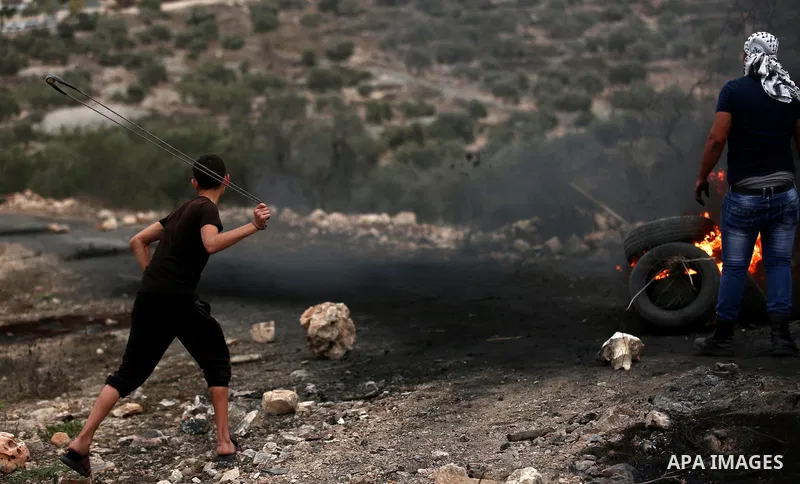 A Palestinian protester uses a slingshot to hurl stones towards Israeli troops during clashes against Israel's Nation State Law, and Israel's plan to demolish the Khan al-Ahmar village, in the village of Kfar Qaddum, nea...