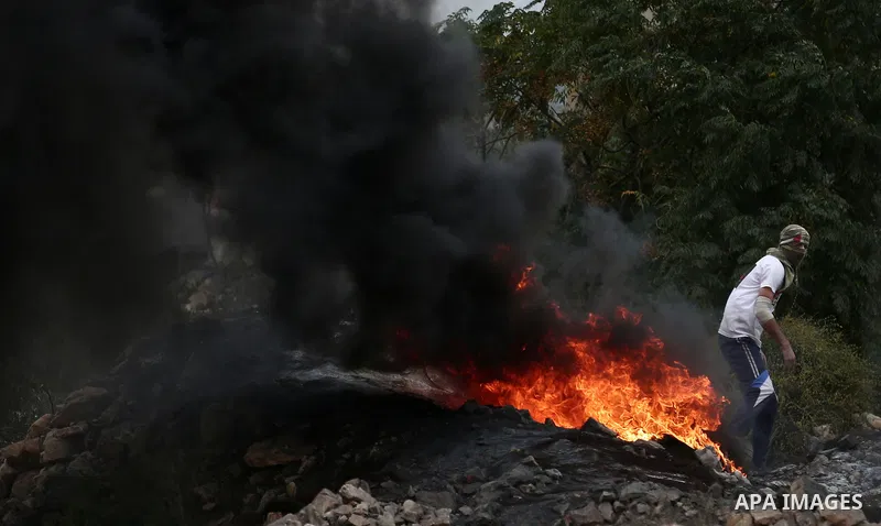 A Palestinian protester burns tires during clashes with Israeli troops against Israel's Nation State Law, and Israel's plan to demolish the Khan al-Ahmar village in the village of Kfar Qaddum, near the West Bank city of...