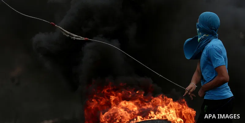 A Palestinian protester uses a slingshot to hurl stones towards Israeli troops during clashes against Israel's Nation State Law, and Israel's plan to demolish the Khan al-Ahmar village, in the village of Kfar Qaddum, nea...