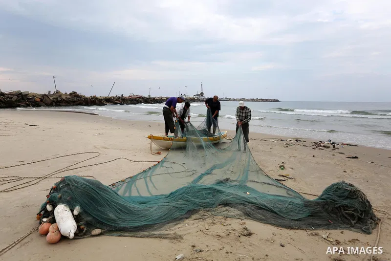 Palestinian fishermen work on their fishing nets on the coast of Gaza City during a rainy day on November 6, 2018. Photo by Ashraf Amra