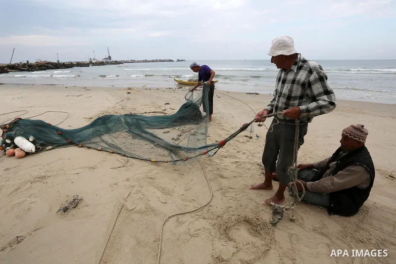 Palestinian fishermen work on their fishing nets on the coast of Gaza City during a rainy day on November 6, 2018. Photo by Ashraf Amra