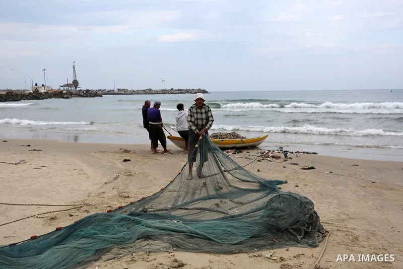 Palestinian fishermen work on their fishing nets on the coast of Gaza City during a rainy day on November 6, 2018. Photo by Ashraf Amra