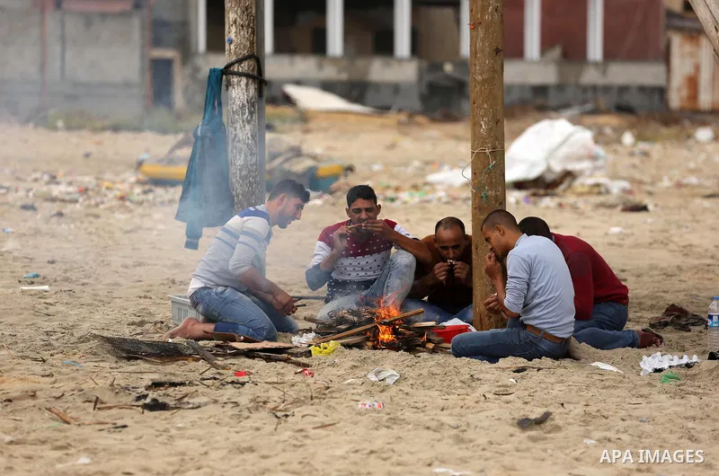 Palestinian fishermen cook food on the coast of Gaza City during a rainy day on November 6, 2018. Photo by Ashraf Amra