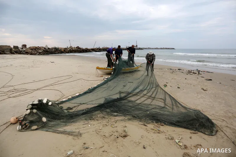 Palestinian fishermen work on their fishing nets on the coast of Gaza City during a rainy day on November 6, 2018. Photo by Ashraf Amra
