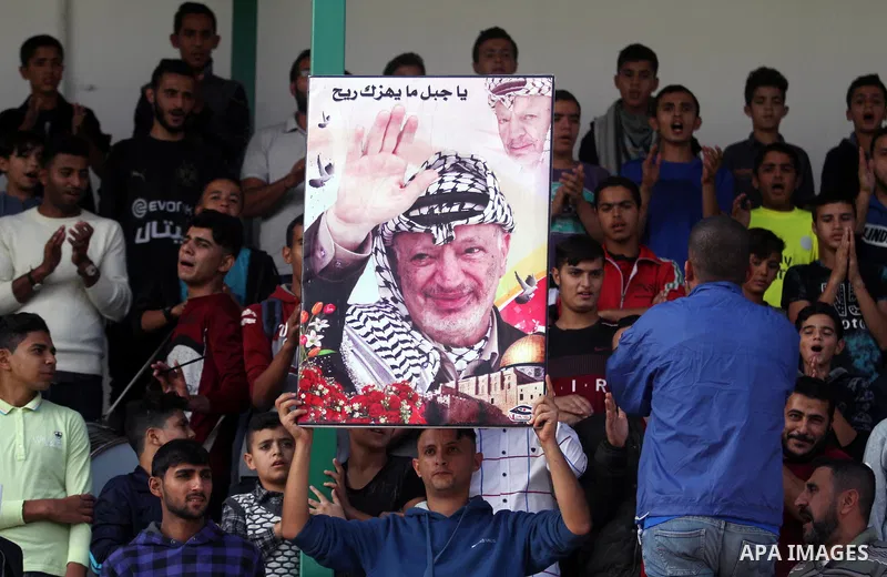 A Palestinian youth holds a pictrue depicting late Palestinian leader Yasser Arafat to mark the 14th anniversary of his death, during a football match between Khadamat al-Shati and Ahly Beit Hanoun, at Yarmouk Stadium in...