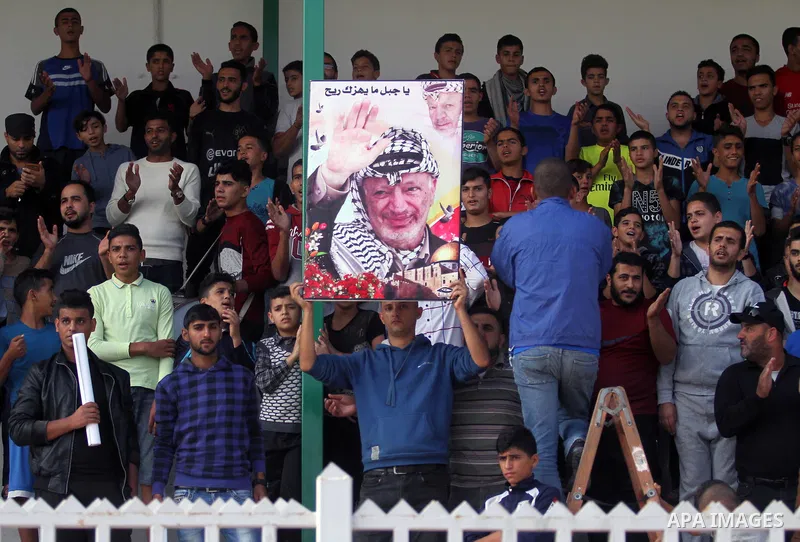 A Palestinian youth holds a pictrue depicting late Palestinian leader Yasser Arafat to mark the 14th anniversary of his death, during a football match between Khadamat al-Shati and Ahly Beit Hanoun, at Yarmouk Stadium in...