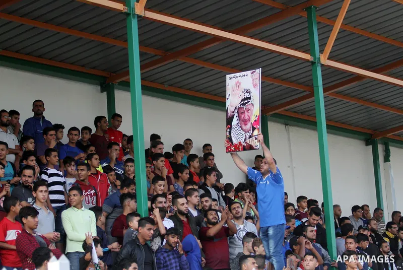 A Palestinian youth holds a pictrue depicting late Palestinian leader Yasser Arafat to mark the 14th anniversary of his death, during a football match between Khadamat al-Shati and Ahly Beit Hanoun, at Yarmouk Stadium in...
