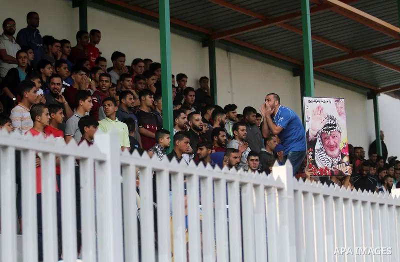 A Palestinian youth holds a pictrue depicting late Palestinian leader Yasser Arafat to mark the 14th anniversary of his death, during a football match between Khadamat al-Shati and Ahly Beit Hanoun, at Yarmouk Stadium in...