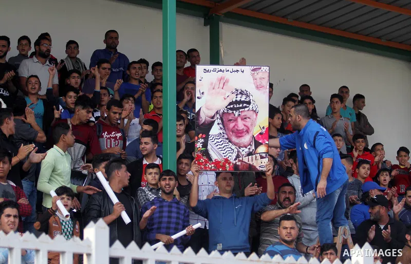 A Palestinian youth holds a pictrue depicting late Palestinian leader Yasser Arafat to mark the 14th anniversary of his death, during a football match between Khadamat al-Shati and Ahly Beit Hanoun, at Yarmouk Stadium in...