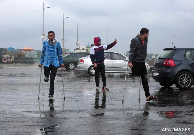 Palestinians with their legs amputated during a protest against Israeli troops, walk at the Gaza sea port during a rainy day in Gaza city on December 20, 2018. Photo by Ashraf Amra