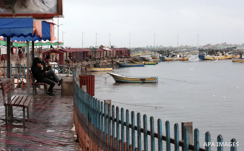 Palestinians sit at the Gaza sea port during a rainy day in Gaza city on December 20, 2018. Photo by Ashraf Amra
