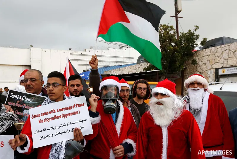 Palestinians dressed as Santa Claus hold signs as they take part in a protest in the West Bank city of Bethlehem on December 23, 2018. Photo by Wisam Hashlamoun