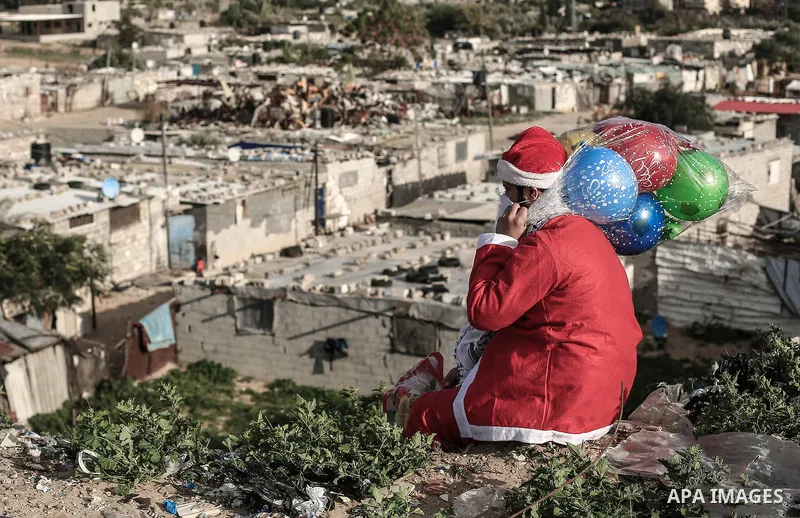 A picture taken on December 27, 2018 shows a Palestinian man Mohammed Abu Hajar, 28, dressed as Santa Claus with gifts bag on his shoulder looks to Nahr al-Bared refugee camp in Khan Younis in the southern Gaza Strip. Ph...
