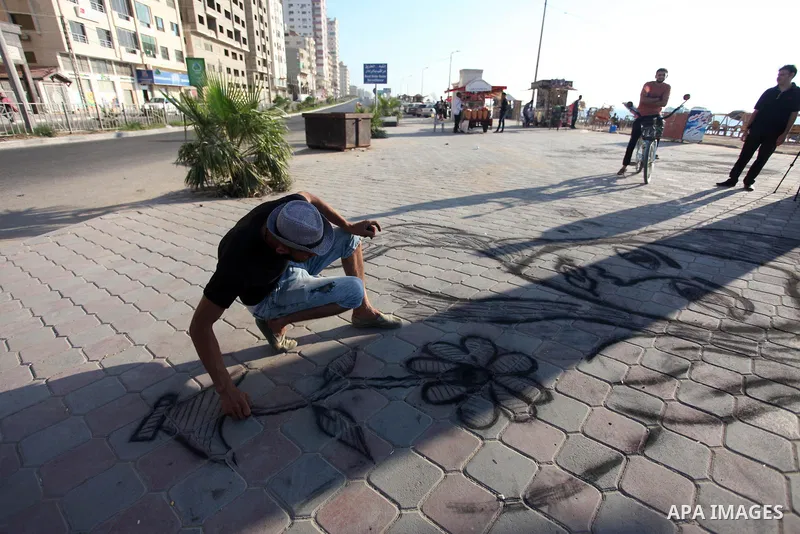 Moawia Ashour, 24, a Palestinian man uses coal to draw on the ground near his street cafe, at the beach of Gaza city, July 30, 2019. Photo by Mahmoud Ajjour
