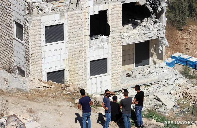Palestinians look as an Israeli bulldozer demolishes a building which does not have the Israeli needed permits on the outskirts of Dura village near the West Bank city of Hebron on September 25, 2019. Israeli bulldozers...
