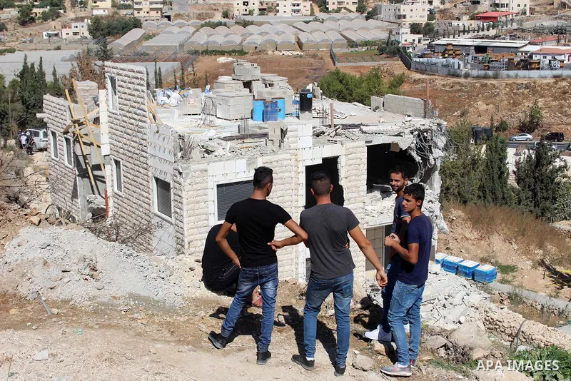 Palestinians look as an Israeli bulldozer demolishes a building which does not have the Israeli needed permits on the outskirts of Dura village near the West Bank city of Hebron on September 25, 2019. Israeli bulldozers...