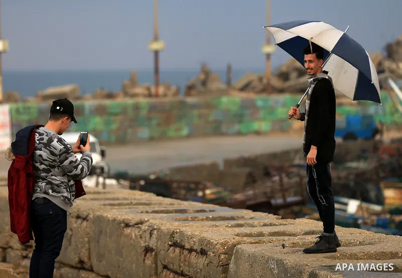 A Palestinian youth holds an umbrella during a rainy day at seaport of Gaza city on December 9, 2019. Photo by Yasser Qudih