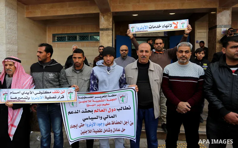 Palestinians hold placards during a rally in support of the headquarters United Nations Relief and Works Agency (UNRWA), at a United Nations-run health center in Dair Al Balah in the center of Gaza strip on December 12,...