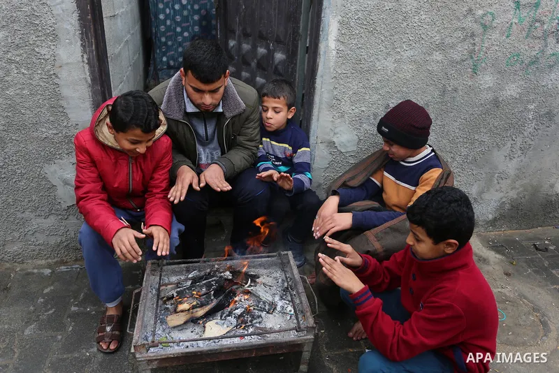 Palestinians warm themselves by a fire during a rainy day in Dair Al Balah in the center of Gaza strip on December 15, 2019. Photo by Ashraf Amra