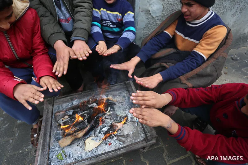 Palestinians warm themselves by a fire during a rainy day in Dair Al Balah in the center of Gaza strip on December 15, 2019. Photo by Ashraf Amra