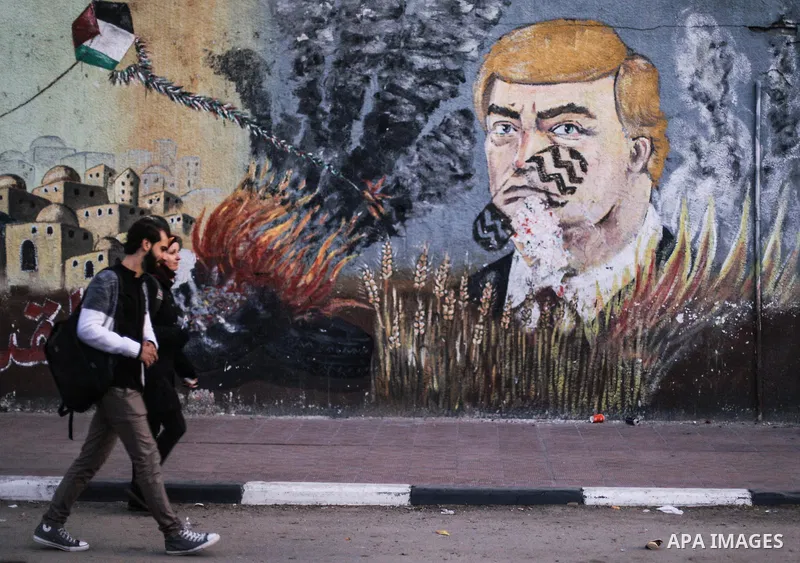 Palestinians walk beside graffiti mural depicting US President Donald Trump with shoe print on his face, in Gaza City, on December 19, 2019. Donald Trump has become only the third US president to be impeached amid a high...