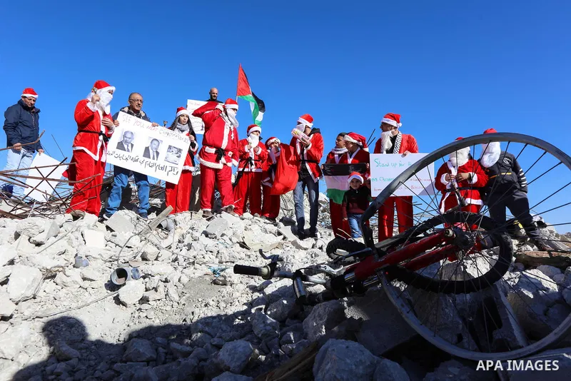 A Palestinian dressed as Santa Claus hands out gifts to children sitting on the remains of a demolished Palestinian house during an anti-Israel protest, in the West Bank city of Bethlehem, on December 23, 2019. Photo by...