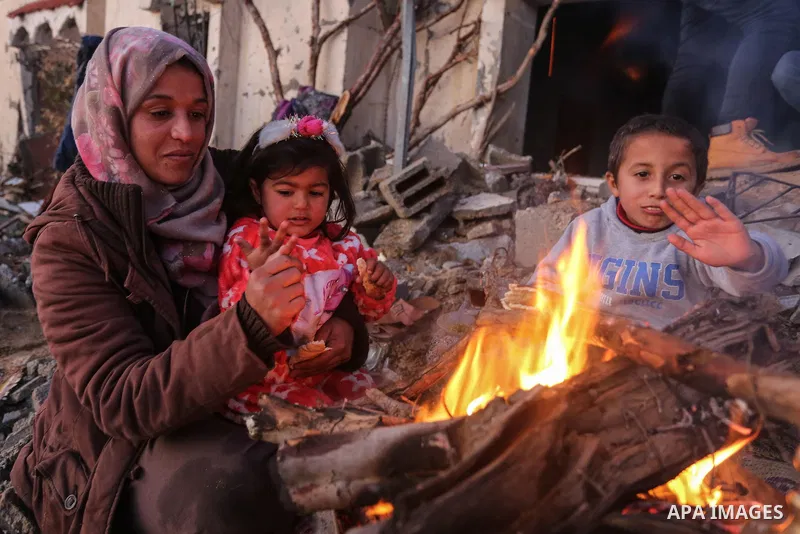 Members of a Palestinian family sit around a fire to warm themselves at the site of their destroyed house, on a cold day, in Khan Youns southern in Gaza city January 10, 2020. Photo by Ashraf Amra