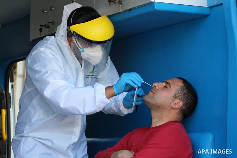 A Palestinian Health Ministry medical professional takes a swab from the nose of a man inside an ambulance during a random testing for COVID-19 coronavirus disease on people entering the West Bank city of Hebron on April...