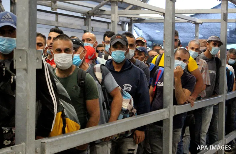 Palestinian labourers wear masks queue to enter Israel through the Mitar checkpoint in the West Bank city of Hebron on June 28, 2020. Photo by Mosab Shawer