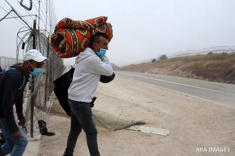 Palestinian labourers wear masks queue to enter Israel through the Mitar checkpoint in the West Bank city of Hebron on June 28, 2020. Photo by Mosab Shawer