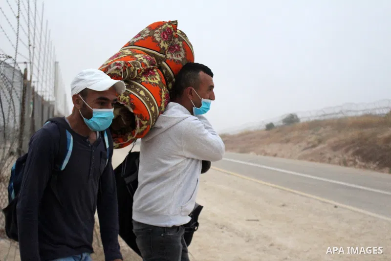Palestinian labourers wear masks queue to enter Israel through the Mitar checkpoint in the West Bank city of Hebron on June 28, 2020. Photo by Mosab Shawer
