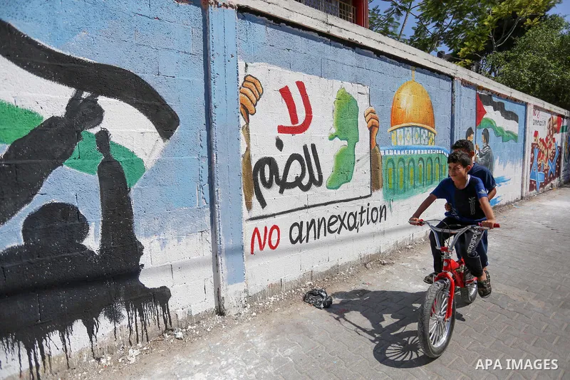 Palestinians walk past a mural against Israel's West Bank annexation plans, in Rafah in the southern Gaza Strip, on July 1, 2020. The government of Israeli Prime Minister Benjamin Netanyahu has said it could begin the pr...