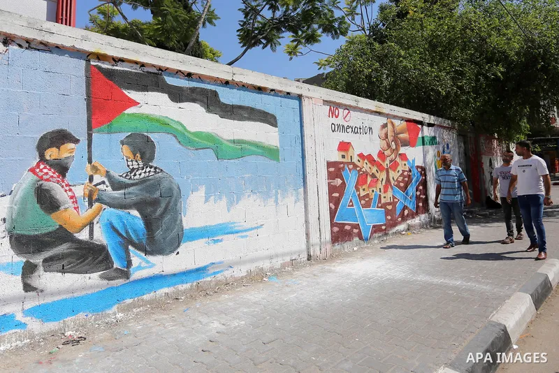 Palestinians walk past a mural against Israel's West Bank annexation plans, in Rafah in the southern Gaza Strip, on July 1, 2020. The government of Israeli Prime Minister Benjamin Netanyahu has said it could begin the pr...