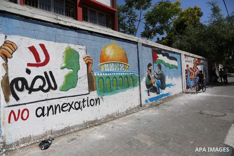 Palestinians walk past a mural against Israel's West Bank annexation plans, in Rafah in the southern Gaza Strip, on July 1, 2020. The government of Israeli Prime Minister Benjamin Netanyahu has said it could begin the pr...
