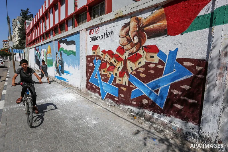 Palestinians walk past a mural against Israel's West Bank annexation plans, in Rafah in the southern Gaza Strip, on July 1, 2020. The government of Israeli Prime Minister Benjamin Netanyahu has said it could begin the pr...