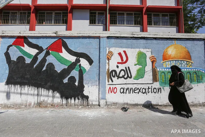 Palestinians walk past a mural against Israel's West Bank annexation plans, in Rafah in the southern Gaza Strip, on July 1, 2020. The government of Israeli Prime Minister Benjamin Netanyahu has said it could begin the pr...