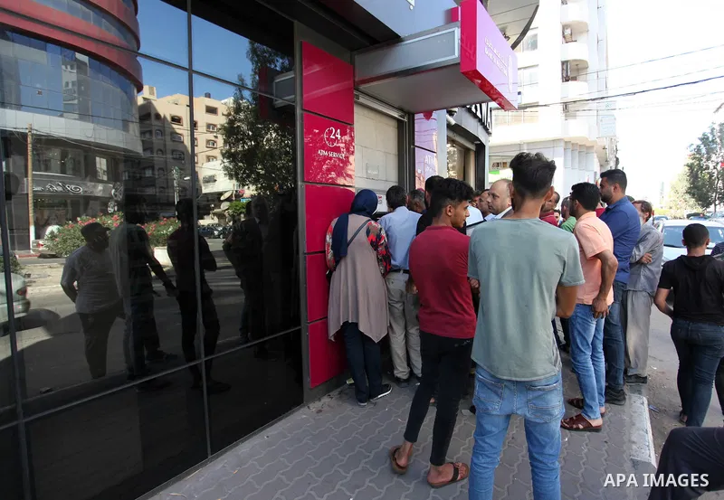 Palestinian Authority employees wait to receive their salaries from an ATM, outside a Palestine Bank in Gaza city, on July 2, 2020. Gazans are strapped for cash and markets are suffering from an unprecedented recession....