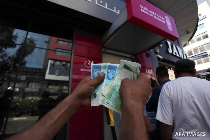Palestinian Authority employees wait to receive their salaries from an ATM, outside a Palestine Bank in Gaza city, on July 2, 2020. Gazans are strapped for cash and markets are suffering from an unprecedented recession....