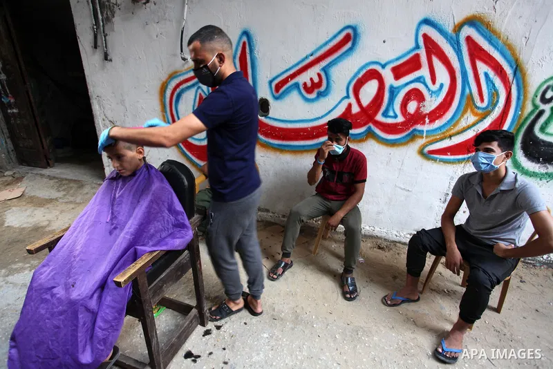 Palestinian barber Sameh Al-Qassas, 27, wears a mask and gloves, shaves for clients free of charge in Gaza city, on August 30, 2020, during a lockdown in the Palestinian enclave due to increasing cases of coronavirus inf...