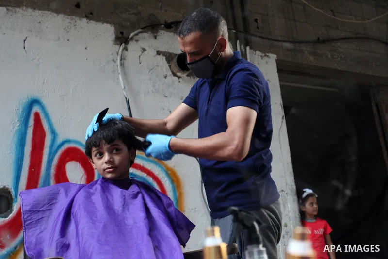 Palestinian barber Sameh Al-Qassas, 27, wears a mask and gloves, shaves for clients free of charge in Gaza city, on August 30, 2020, during a lockdown in the Palestinian enclave due to increasing cases of coronavirus inf...
