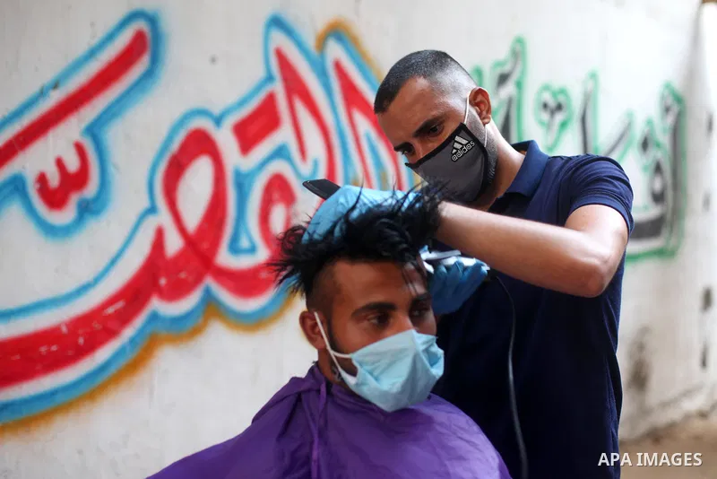 Palestinian barber Sameh Al-Qassas, 27, wears a mask and gloves, shaves for clients free of charge in Gaza city, on August 30, 2020, during a lockdown in the Palestinian enclave due to increasing cases of coronavirus inf...