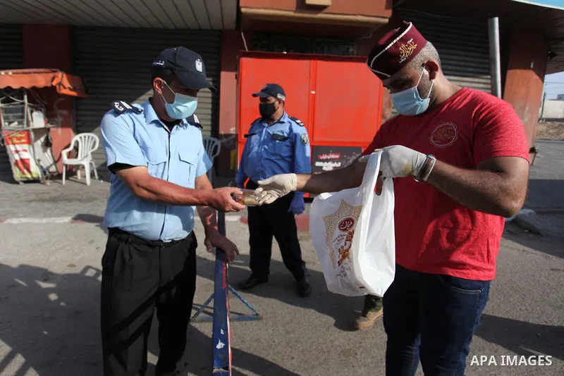 A Palestinian seller distributes sweets to me Palestinian policemen during the imposed lockdown to mitigate virus outbreak in the Gaza Strip, in Gaza city on August 31, 2020. Photo by Mahmoud Ajjour