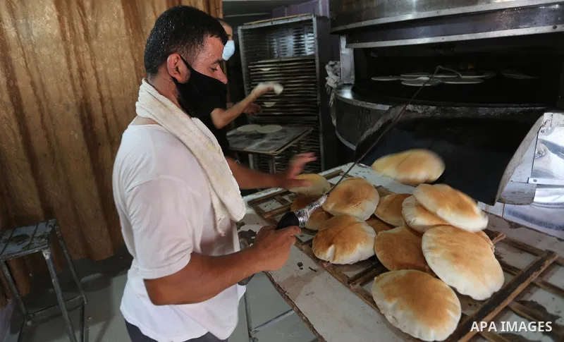 Palestinian men wear protective face masks, as they bake a traditional bread, during a lockdown following the outbreak of the coronavirus disease (COVID-19), in Dair Al Balah in the central of Gaza Strip, on September 6,...