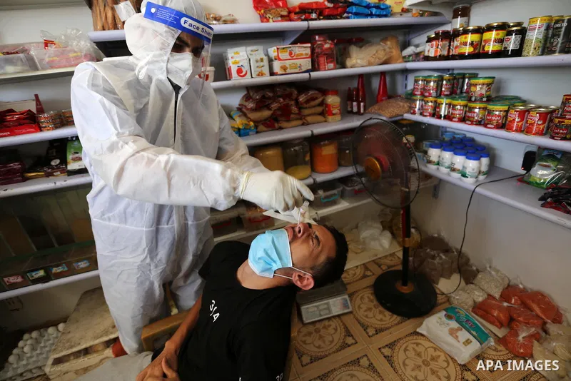 A Palestinian midical wearing protective gear, takes a swab sample from a man during a COVID-19 screening campaign in Deir Al-Balah, in the central Gaza Strip, on September 24, 2020. Photo by Ashraf Amra