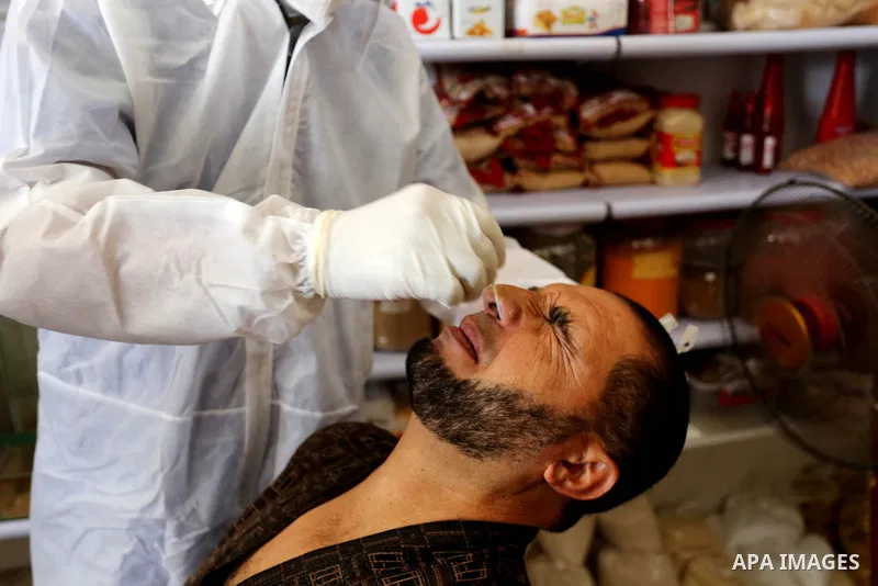 A Palestinian midical wearing protective gear, takes a swab sample from a man during a COVID-19 screening campaign in Deir Al-Balah, in the central Gaza Strip, on September 24, 2020. Photo by Ashraf Amra