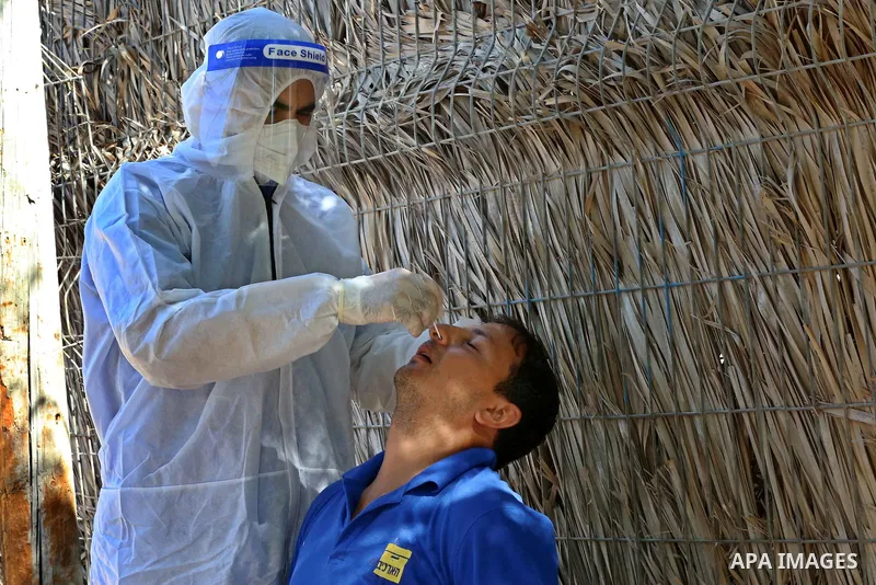 A Palestinian midical wearing protective gear, takes a swab sample from a man during a COVID-19 screening campaign in Deir Al-Balah, in the central Gaza Strip, on September 24, 2020. Photo by Ashraf Amra