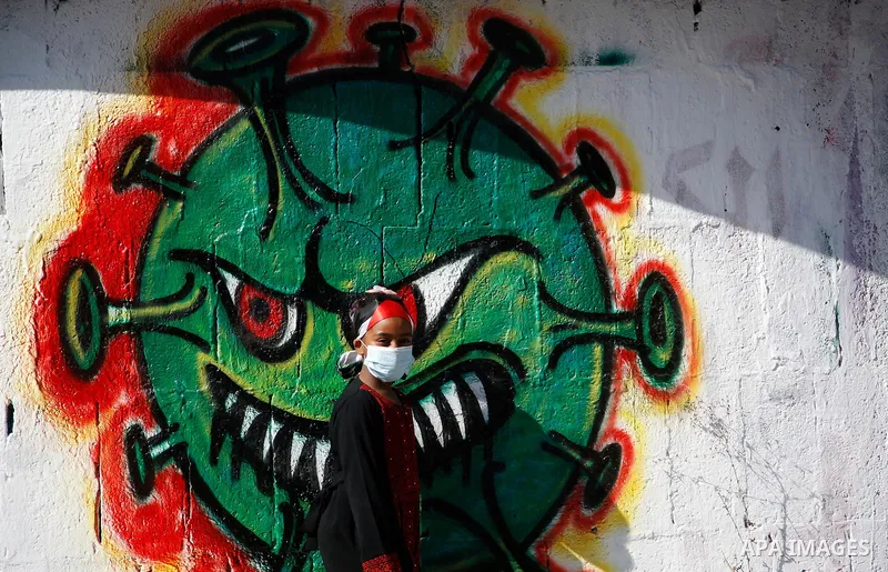 A Palestinian girl wearing protective face mask, walks past a mural, amid concerns about the spread of the disease (COVID-19), in Gaza City on October 5, 2020. Photo by Osama Baba